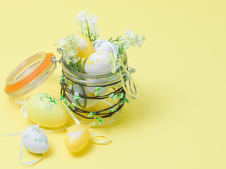 A glass jar with buds in which are decorative Easter eggs, spring flowers and willow buds on a yellow.