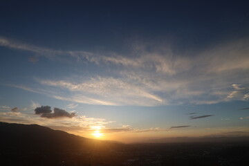 Golden sunset over hills and scattered clouds.