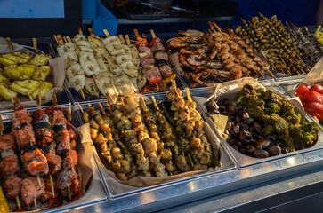 Variety of skewered foods displayed at market including vegetables seafood and meats grilled and presented for outdoor catering. Tempting and visually appealing display of delicious culinary options
