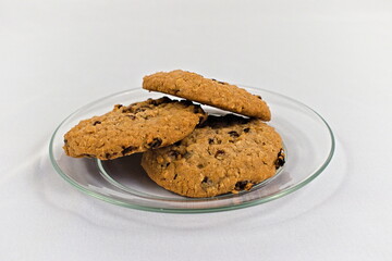 Three delicious oatmeal cookies stacked on top of each other sitting on a glass plate with a white background.