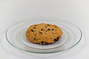 A single delicious oatmeal cookie sitting on a glass plate with a white background.