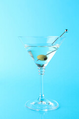 Martini cocktail with olive in glass on light blue background