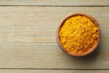 Turmeric powder in bowl on wooden table, top view. Space for text