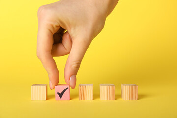 Woman taking pink cube with check mark on yellow background, closeup