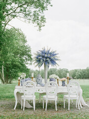 Elegant outdoor dining setup with floral arrangements and white chairs in a serene park environment