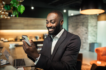 Smiling young black businessman using smartphone in modern office
