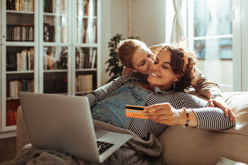 Lesbian couple online shopping with credit card on laptop at home