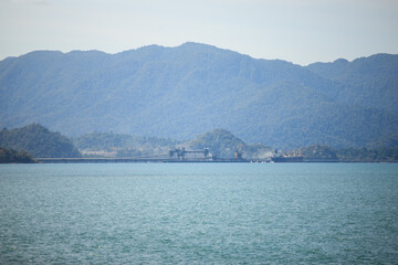 Distance view of cement quarry with mountainous background. Gravel conveyor machine. Gravel transportation ship by the harbour. Mining industry.
