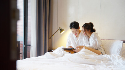 Asia people young adult man woman using social media relax smile laugh fun sitting on cozy home bed hotel room enjoy flirt talk date day. Joy tender happy asian lovers wife just married sweet newlywed © ChayTee