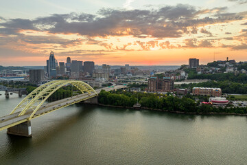 Naklejka premium Highway traffic in Cincinnati, Ohio on Daniel Carter Beard Bridge with brightly illuminated high skyscraper buildings in downtown district. American city with business financial district at sunset