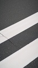 Fototapeta premium Close-up view of freshly marked pedestrian crossings with grey asphalt textures and contrasting white lines set against a cracked asphalt backdrop