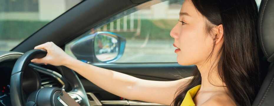 Smiling Asian woman is driving a car and use smartphone to view a map showing travel route.