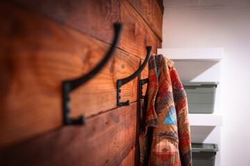 A wooden wall in a warm cabin with three hooks on it. A red and brown jacket is hanging on the last hook