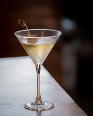A classy martini glass with a green olive on top. The glass is full and the olive is floating on top of the drink