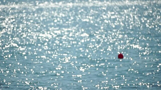 Water, Sun, Reflection: Close-up shot of shimmering water surface reflecting sunlight, with a small red object floating in the distance.