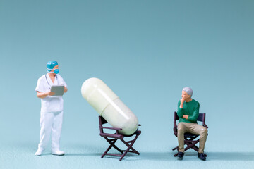 Miniature figurine doctor, a patient, and an oversized pill seated on a chairs, symbolizing medical...