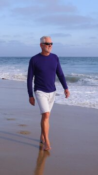 A mature 66 year old man enjoying a walk at the beach in Southern California. Vertical Video.