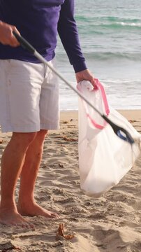 Mature 66 year old man picking up trash from a beach in Southern California. Vertical Video.
