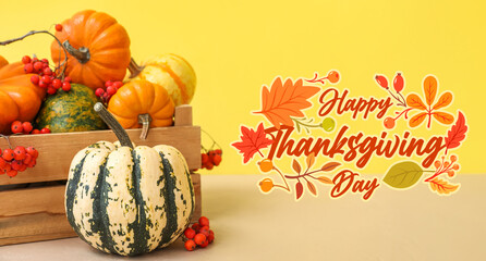 Wooden box with Halloween pumpkins and rowan berries on table against yellow background