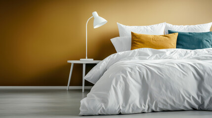A serene bedroom scene featuring a white bedspread, colorful pillows, and a stylish lamp against a warm brown wall.