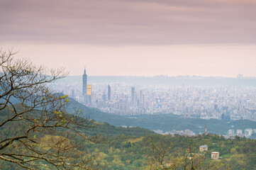 Naklejka premium Overlooking the misty Taipei cityscape from Dajian Mountain. The city lights twinkle softly amidst the haze, while the sky above is painted with delicate hues of pink and purple. Xizhi, Taiwan.