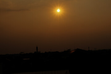 The atmosphere approaching dusk, the sun is above the silhouette of the houses in the city with the orange sky