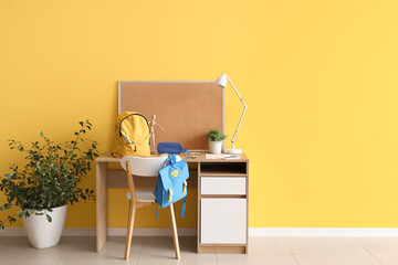 Workspace with school supplies and backpack near yellow wall