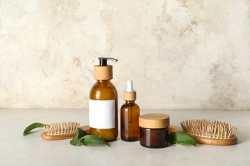 Composition with bottles of shampoo and hair brushes on table near beige grunge wall