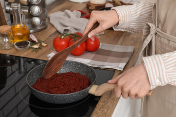 Young woman cooking tomato paste on stove in kitchen