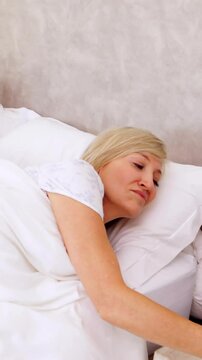 Peaceful couple sleeping in bed with woman turning off alarm