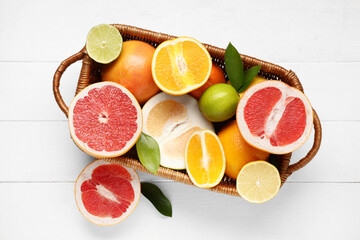 Wicker basket with tasty citrus fruits on white wooden background