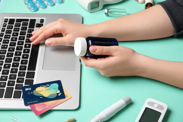 Female hands with bottle of pills, modern laptop, credit cards and medical supplies on color background, closeup