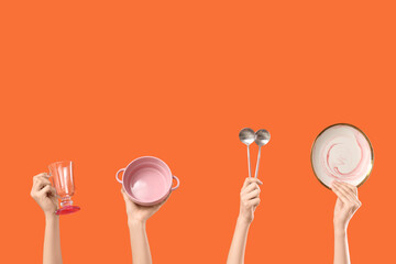Female hands with plate, bowl, glass and spoons on orange background