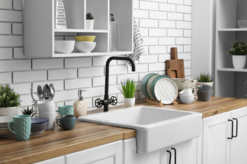 Wooden kitchen counter with sink, clean dishes and shelving unit hanging on light brick wall