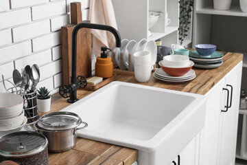 Ceramic sink and clean dishes on wooden counter near light brick wall