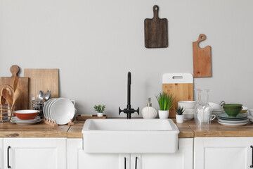 Wooden counter with stylish ceramic sink, clean dishes and kitchen utensils near grey wall