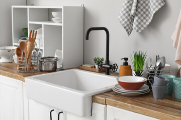 Ceramic sink, clean dishes, and shelving unit on wooden kitchen counter