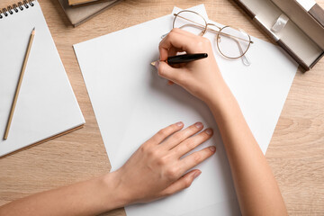 Female hands with blank paper sheets, pen, eyeglasses and stationery on wooden background, closeup