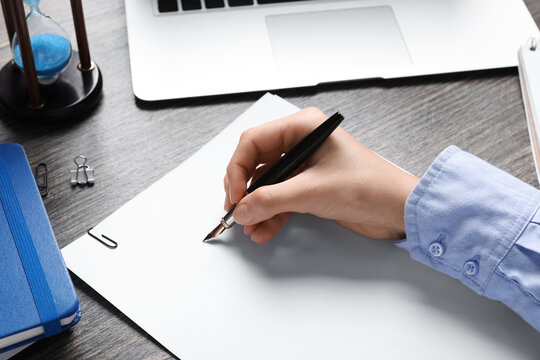 Female hand with blank paper sheet, fountain pen, laptop and hourglass on wooden table, closeup