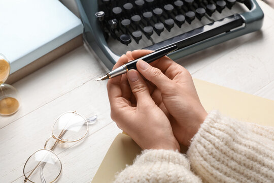 Female hands with fountain pen, notebook, eyeglasses and typewriter on light wooden table, closeup