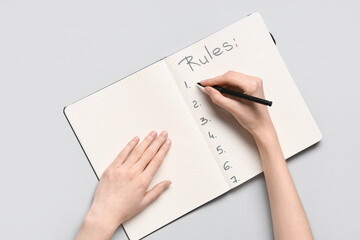 Woman writing list of rules in notebook on light background