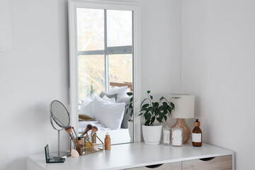 Dressing table with cosmetic products and lamp near white wall in bedroom