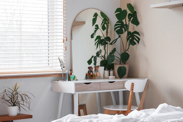 Dressing table with houseplant and cosmetic products in interior of bedroom