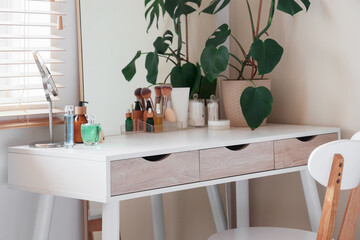 Dressing table with houseplant and cosmetic products in interior of bedroom
