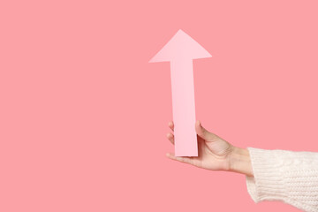 Female hand with paper arrow pointing at something on pink background
