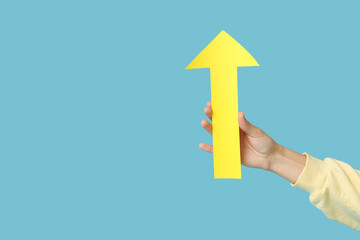 Female hand with paper arrow pointing at something on blue background