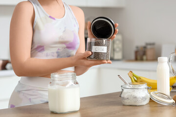 Sporty young woman with chia seeds and yogurt at table in kitchen, closeup