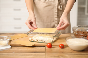 Beautiful mature woman cooking delicious lasagna at table in kitchen, closeup