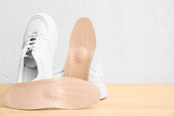 Sneakers with beige orthopedic insoles on wooden table near light wall