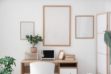 Workplace with laptop and blank posters on white wall in room